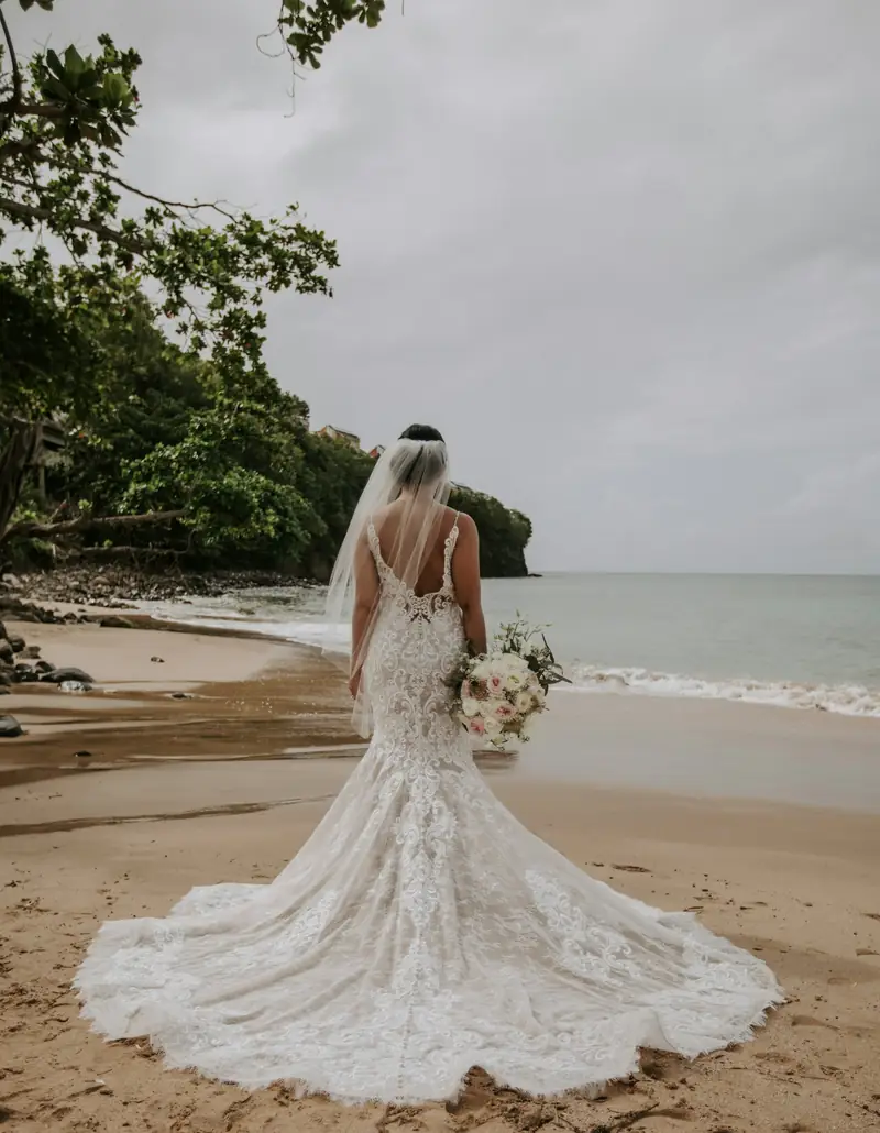 Bride in a lace mermaid gown standing where the forest meets the beach