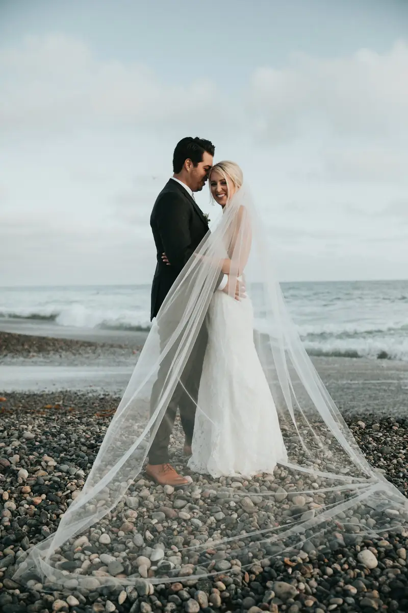 Bride with a long veil on a pebble beach