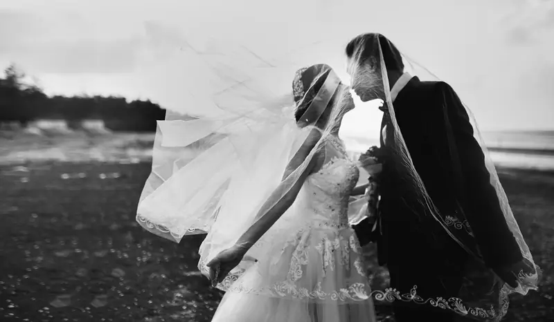 Black and white portrait of a couple kissing under a veil