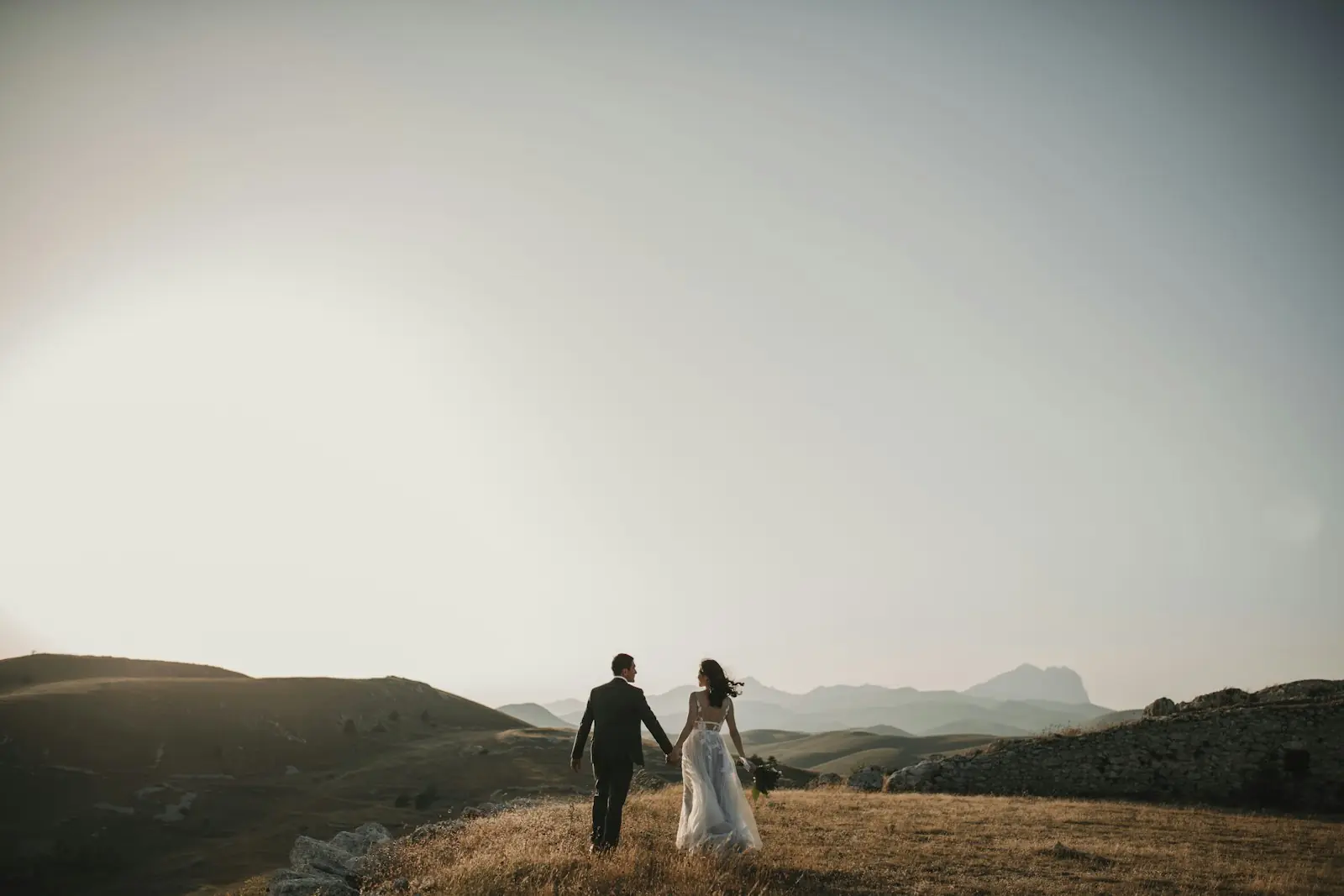 Couple walking hand in hand across golden hills